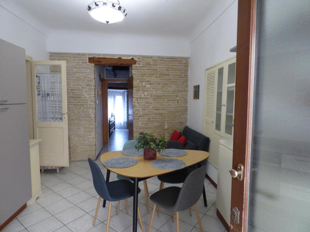 A dining area features a round wooden table surrounded by four chairs, set against a wall of exposed brick. A small potted plant adds a touch of greenery. Natural light enters through a nearby doorway, enhancing the bright atmosphere of the space.