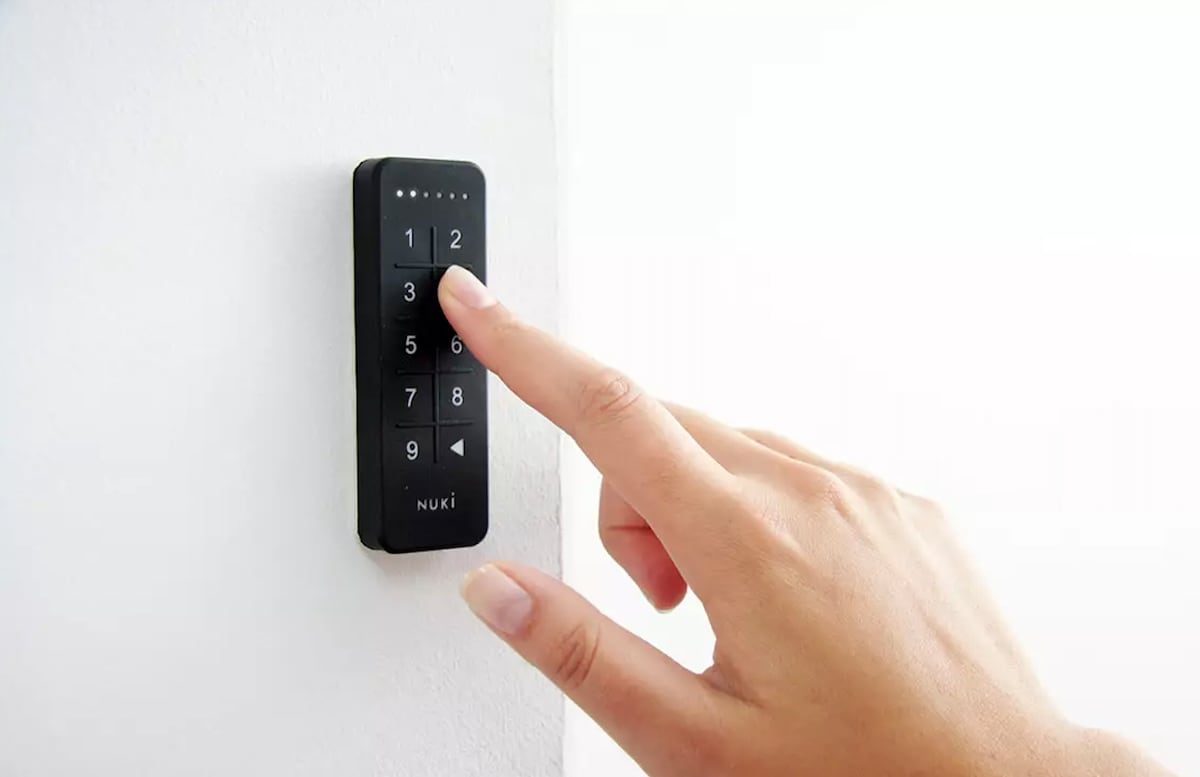 A close-up of a keyless entry system is shown, featuring a black panel with a numerical keypad. A finger is seen pressing one of the buttons, emphasizing its modern technology and ease of use.