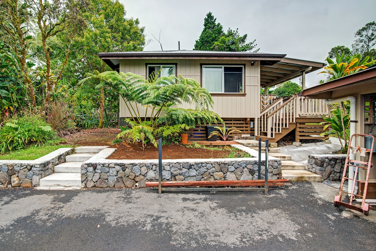 The exterior of the guesthouse features a cozy porch and is surrounded by lush greenery. A planted area is situated in front, complemented by stone pathway steps. The driveway is paved, with a stone border visible along the garden beds.