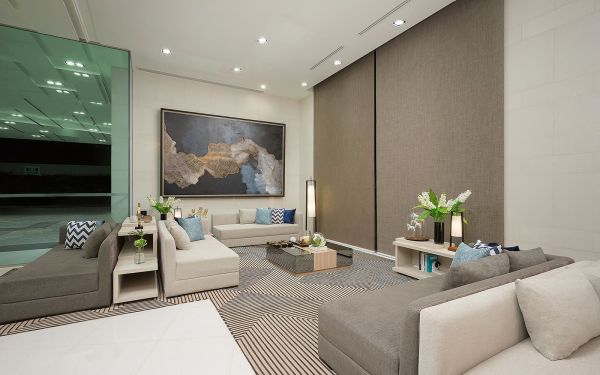 A contemporary lounge area is presented with neutral-toned sofas arranged around a coffee table. An oversized artwork adorns one wall, while soft lighting is provided by floor lamps. Fresh flowers are placed on the table, and a striped rug adds texture to the space.