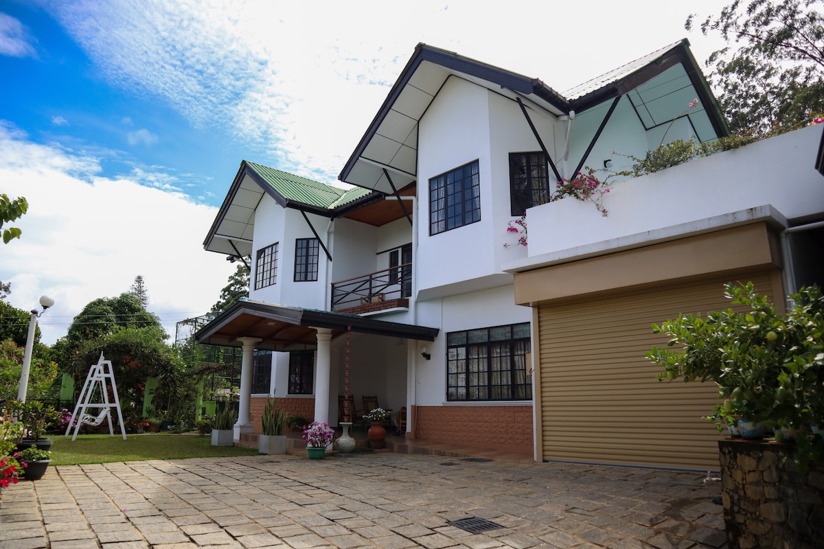 The exterior of the bungalow features a modern design with a sloping roof and large windows. A spacious stone patio leads to the entrance, flanked by potted plants. The landscaped garden includes a swing set visible in the background, enhancing the serene outdoor atmosphere.