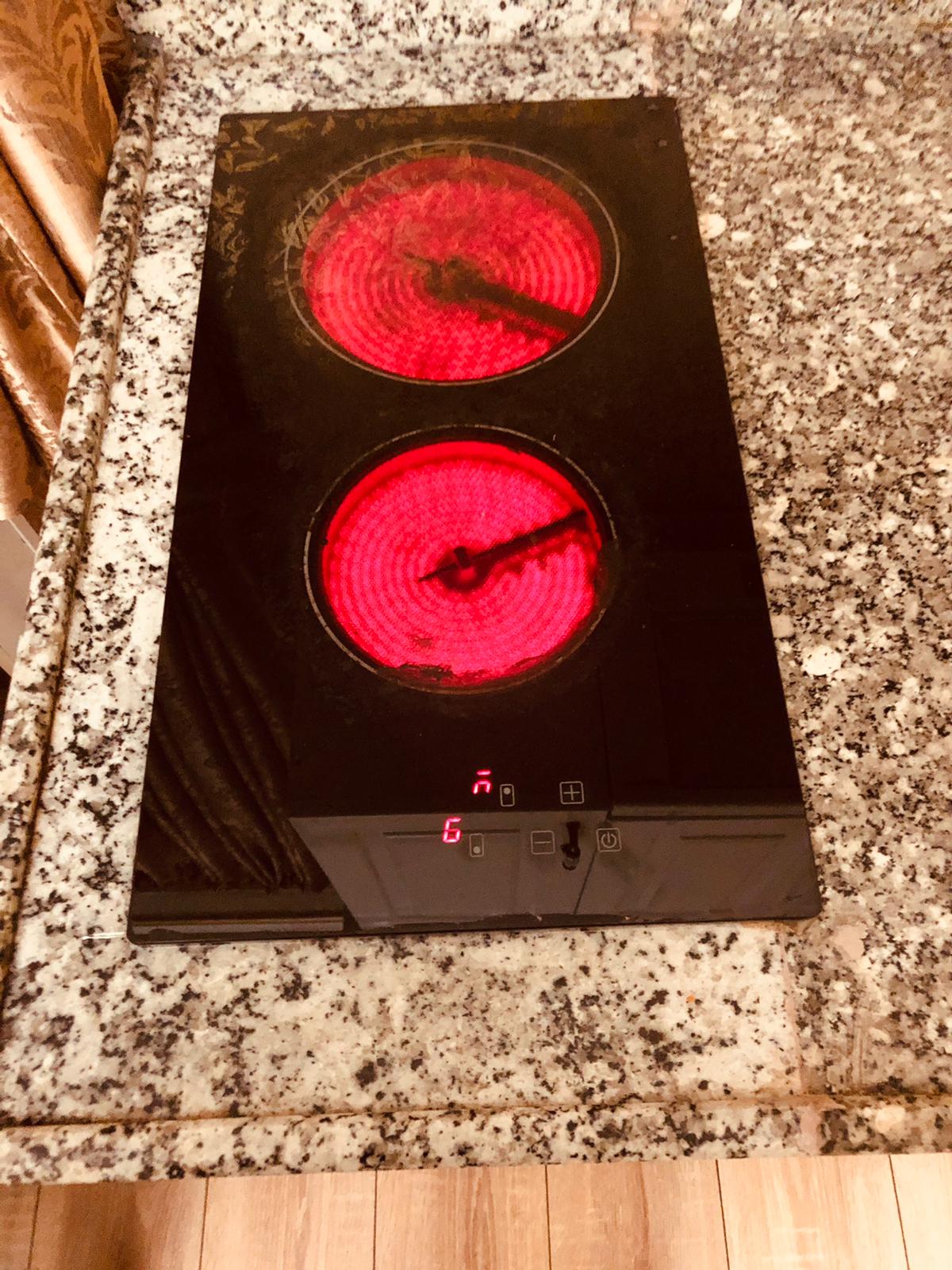 A sleek, black cooking surface is shown, featuring two heating elements glowing in red. The surface is set against a speckled granite countertop, and a control panel with buttons is visible below the cooking area.