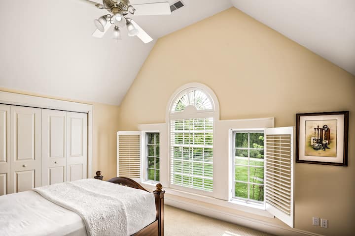 Chambre principale dans la suite avec lit queen size, plafonds voûtés et immenses fenêtres donnant sur le domaine.