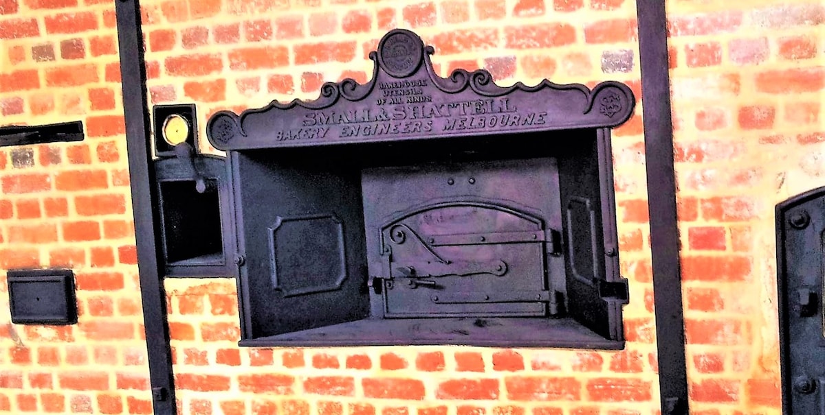 A historic brick oven is showcased, featuring intricate metal detailing and an engraved sign that reads 'Small's Slaughter.' The oven is framed by warm-toned brickwork, highlighting the craft of the original bakery.