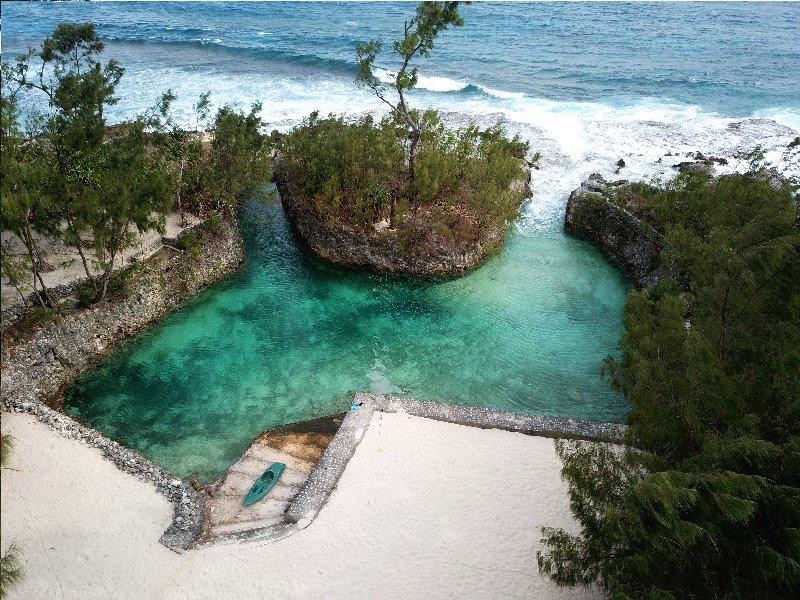 A serene lagoon is surrounded by rocky formations and lush greenery. The crystal-clear waters are set against a backdrop of sandy shores and gentle waves. A small boat rests on the sandy edge, inviting relaxation and exploration.