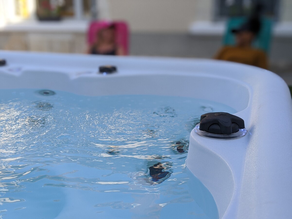 The image captures a close-up of a jacuzzi, featuring bubbling water that reflects light. In the background, two loungers are visible, suggesting a relaxed outdoor setting for leisure and socializing.
