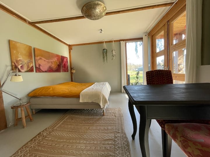 Eneo la kulala lililo karibu na milango ya Kifaransa ya kiti kilichofunikwa na kitanda cha bembea na mwonekano usio na kizuizi wa yadi na mashamba.