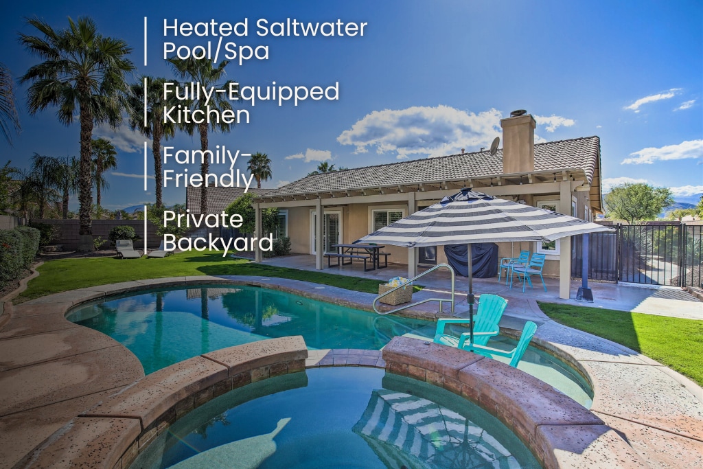 A serene backyard is featured, showcasing a heated saltwater pool and spa surrounded by palm trees. A shaded patio area with an umbrella offers seating. The home, with a neutral facade, is seen in the background, providing a spacious and inviting outdoor environment.