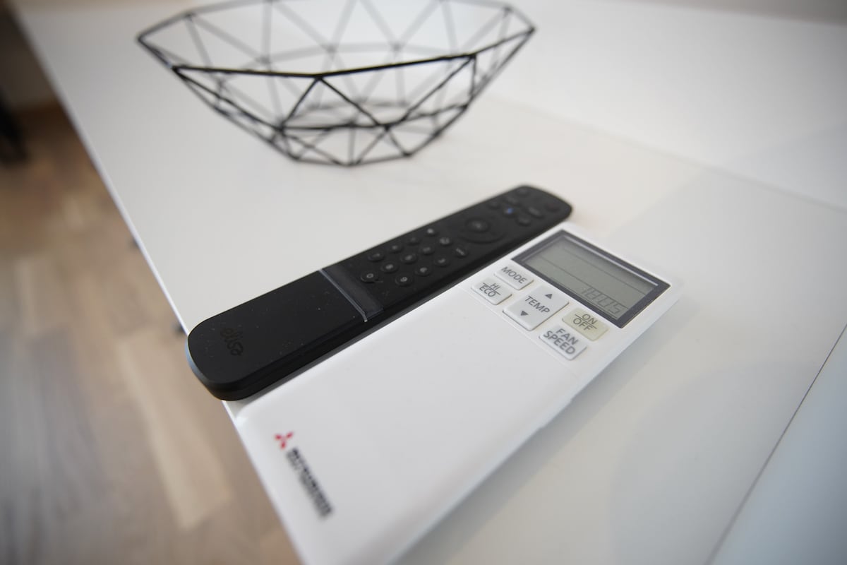 A modern coffee table displays a black remote control alongside a white temperature control unit. A geometric wire bowl is positioned in the background, contributing to the minimalist design of the space.
