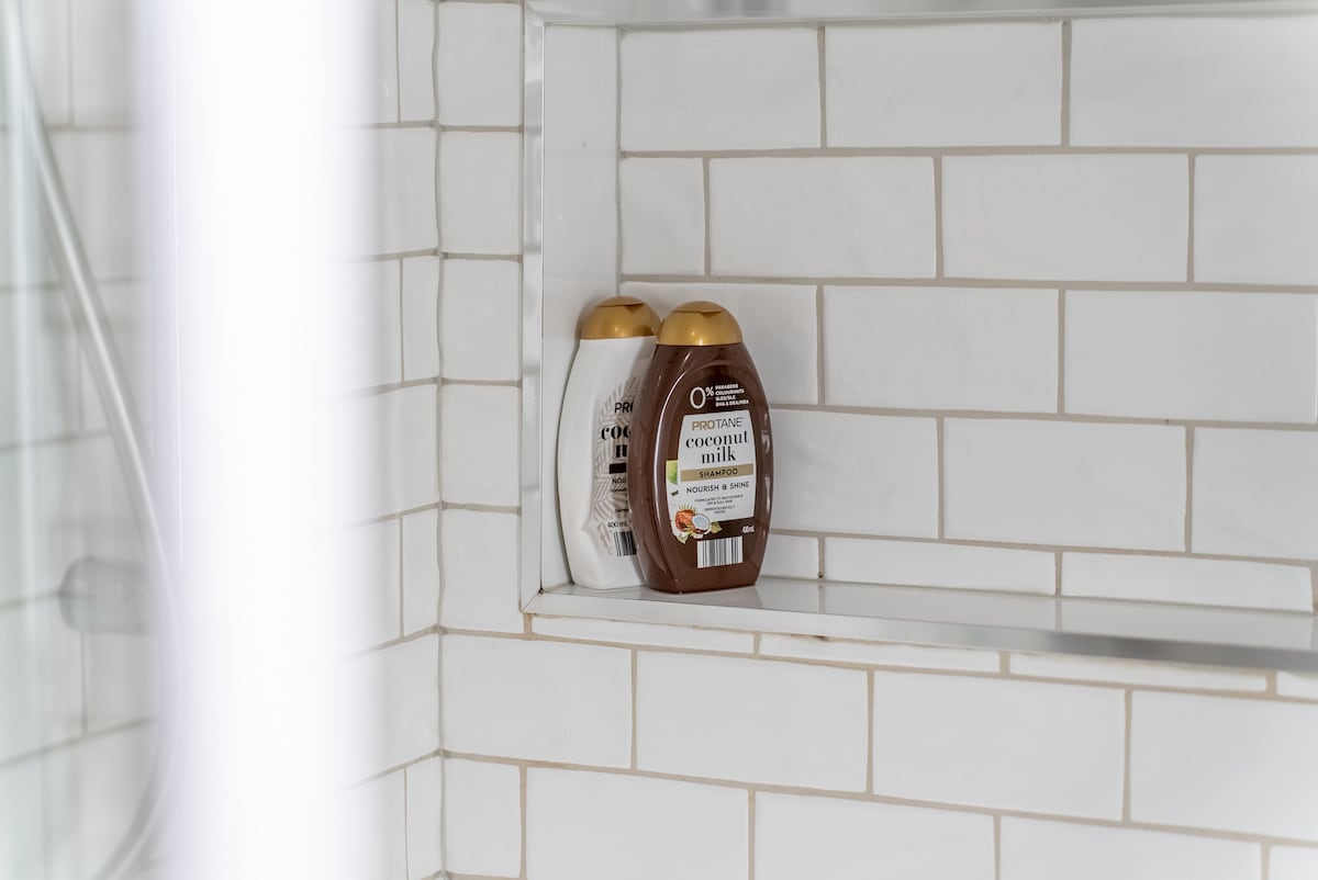 A neatly arranged shower niche holds two bottles of shower gel, one labeled with a cream-colored cap and the other with a brown cap. The backdrop consists of white subway tiles, creating a clean and modern aesthetic.
