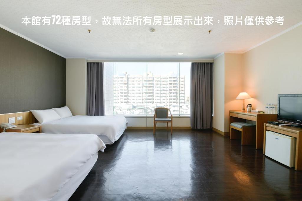 The room features two spacious beds positioned near a large window, allowing natural light to brighten the space. A wooden desk and chair are arranged against the wall, providing a workspace. Light-colored walls and dark wood flooring enhance the modern, clean aesthetic.