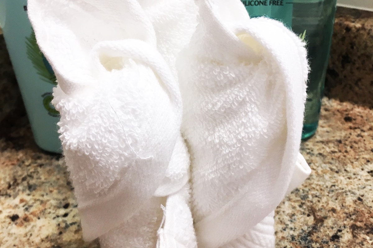 Two neatly rolled white towels are positioned on a granite countertop, complemented by a bottle of silicone-free shampoo in the background. The soft texture of the towels contrasts with the smooth surface of the stone, suggesting a clean and organized space.