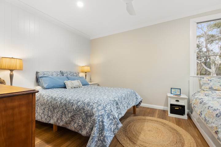 Bedroom 2 offers serene north and west-facing bush views. It's furnished with a queen bed and a single with trundle, sleeping up to 4. Complete with a ceiling fan, ample storage.