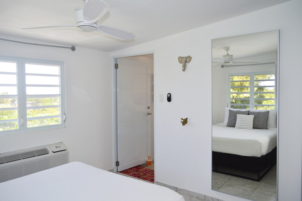 El dormitorio de #4 Mango Mountain siempre está diseñado con sábanas blancas frescas, mantas y toallas de baño. ¿Necesitas más? Avisadnos. Disfruta del cómodo colchón tamaño queen y de las vistas al amanecer sobre el árbol de Ceiba.
