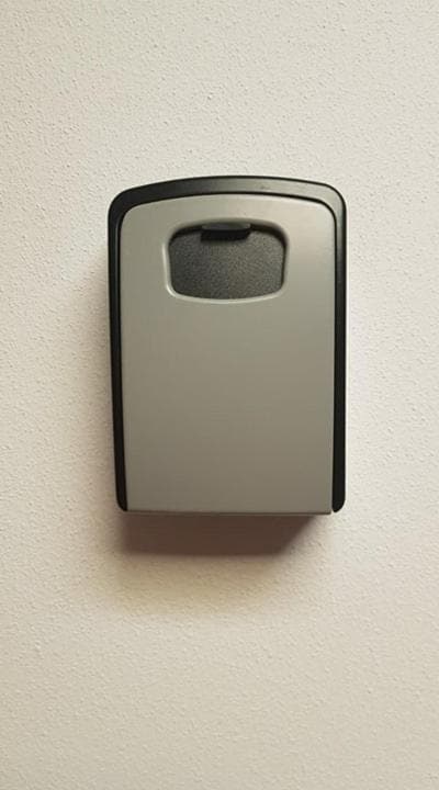 A wall-mounted key card holder is displayed, featuring a sleek, rectangular design in metallic gray and black. The card slot is positioned at the top, and the holder is affixed to a light-colored wall, emphasizing its clean lines and minimalistic style.