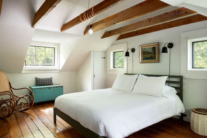 Sun-drenched primary suite featuring a plush king bed, dual closets, and a versatile drop-leaf desk/vanity—all wrapped in the cozy, intimate charm of a classic historic home.