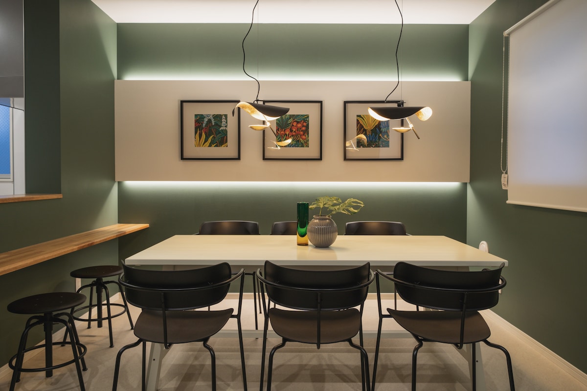 A dining area is presented with a white table surrounded by six black chairs. Two framed artworks add color to the wall, while stylish pendant lights provide illumination. A minimalist wooden bench runs alongside, enhancing the room's modern aesthetic.
