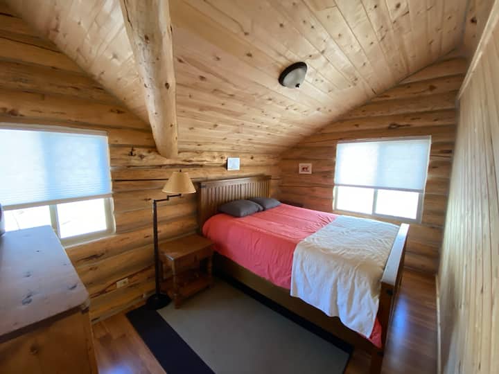 Спалня на горния етаж #1.  Двойно легло.  Прозорецът гледа към памучни дървета и пасища.  