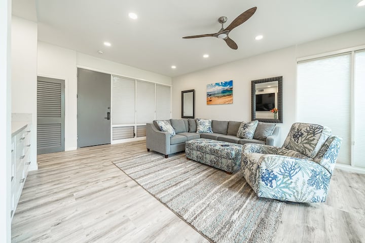 The living room features a modern remodel and a  comfortable queen sleeper sectional, storage ottoman, recliner, new entertainment center with 84" smart TV, large windows with new cellular window coverings to let the island light in. 