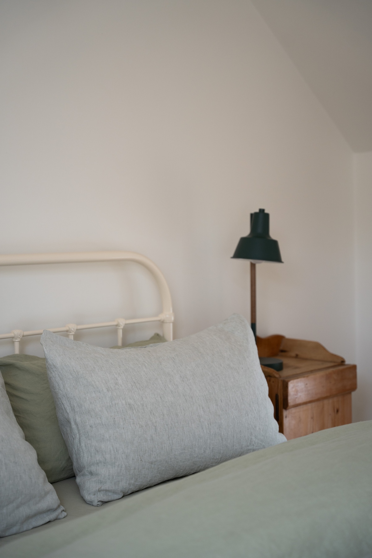 A cozy sleeping area is presented with a king-sized bed featuring soft linens in muted tones. An elegant lamp stands beside the bed, and a wooden chest adds a touch of warmth to the minimalist decor.