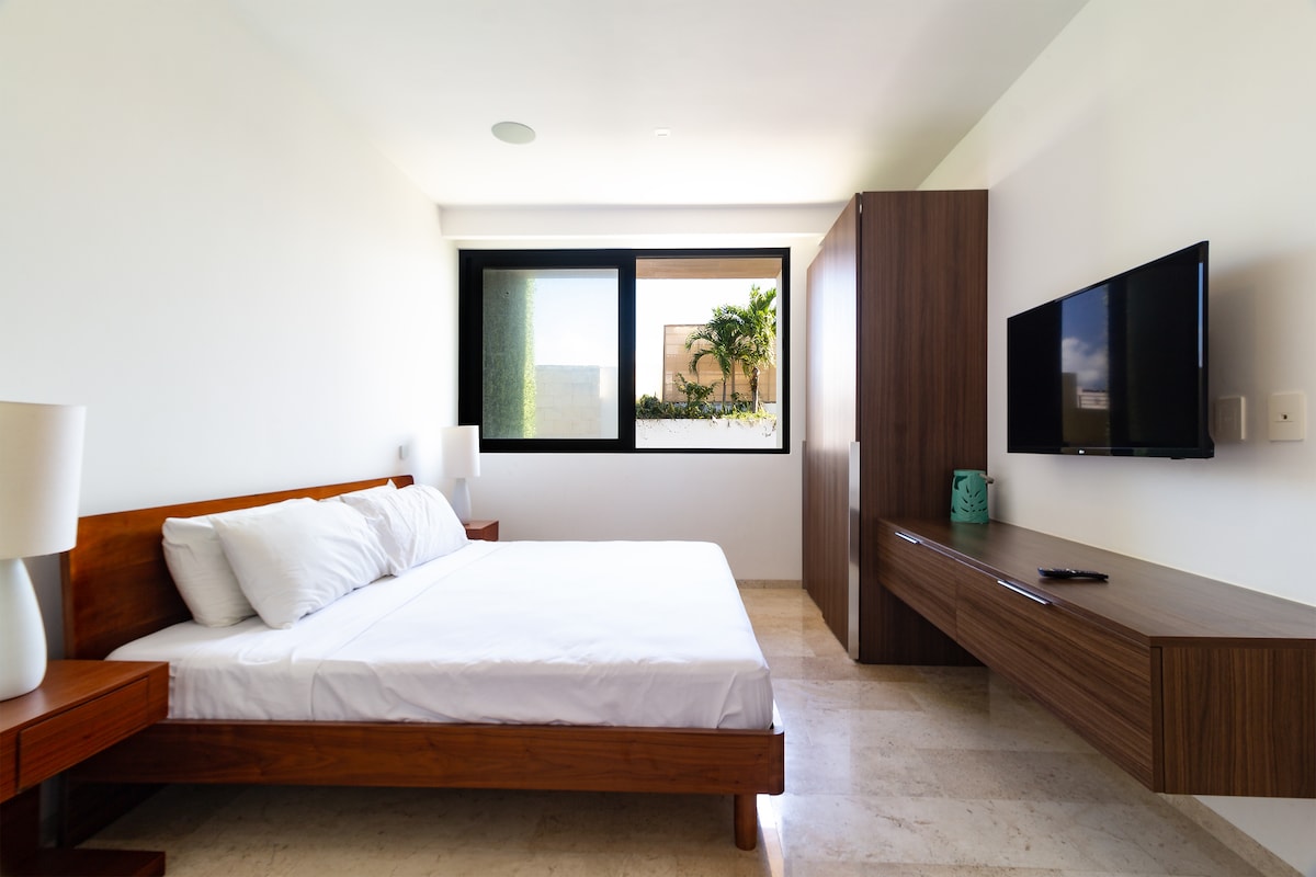 Au centre de la chambre se trouve un grand lit king size confortable, orné de draps blancs et de coussins décoratifs dans des tons doux.