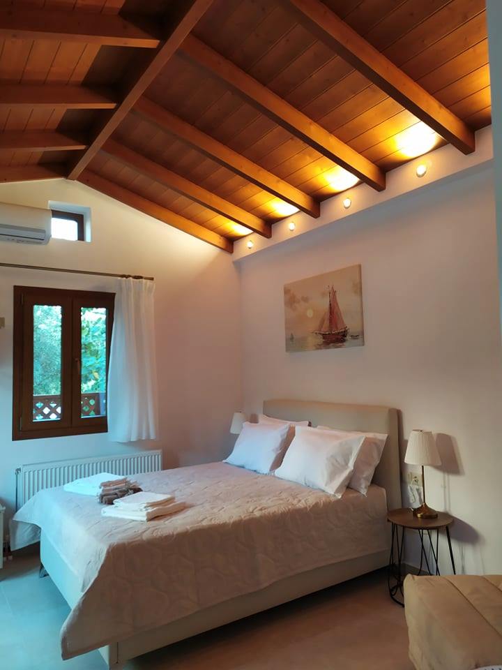 A cozy sleeping area features a spacious bed with crisp white linens and neatly arranged towels. Soft lighting illuminates the room, highlighting the wooden ceiling and a window with simple white curtains. A small bedside table complements the arrangement.