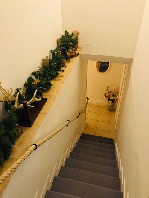 Stairs leading downward are lined with a garland, enhancing the clean and simple design. A decorative touch is provided by small ornaments displayed on the ledge. The bright tiled floor is visible at the bottom, along with a flower arrangement near the wall that adds a subtle hint of color.