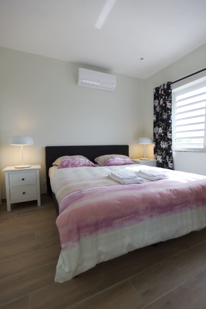 Chumba chetu kikuu cha kulala chenye nafasi kubwa kina kiyoyozi kwa ajili ya kulala vizuri usiku. Unaweza pia kutazama televisheni hapa kitandani