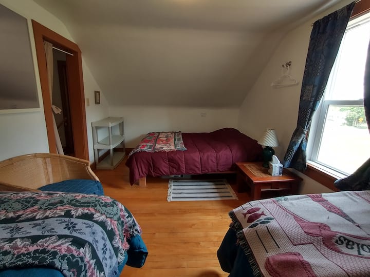 חדר שינה עם מיטה מלאה ושתי מיטות נפרדות ודוכני לילה עם מנורות. 