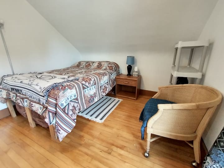 חדר שינה עם מיטה מלאה ומיטה זוגית מתחת. שידת לילה עם מנורה.