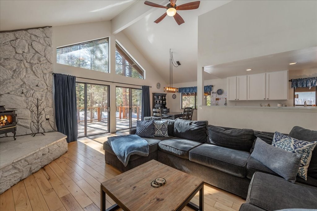 A spacious living area is highlighted by a large sectional sofa, offering comfort and ample seating. A stone fireplace provides a cozy focal point, while tall windows bring in natural light and views of the surrounding trees. A coffee table sits centrally, enhancing the inviting setting.