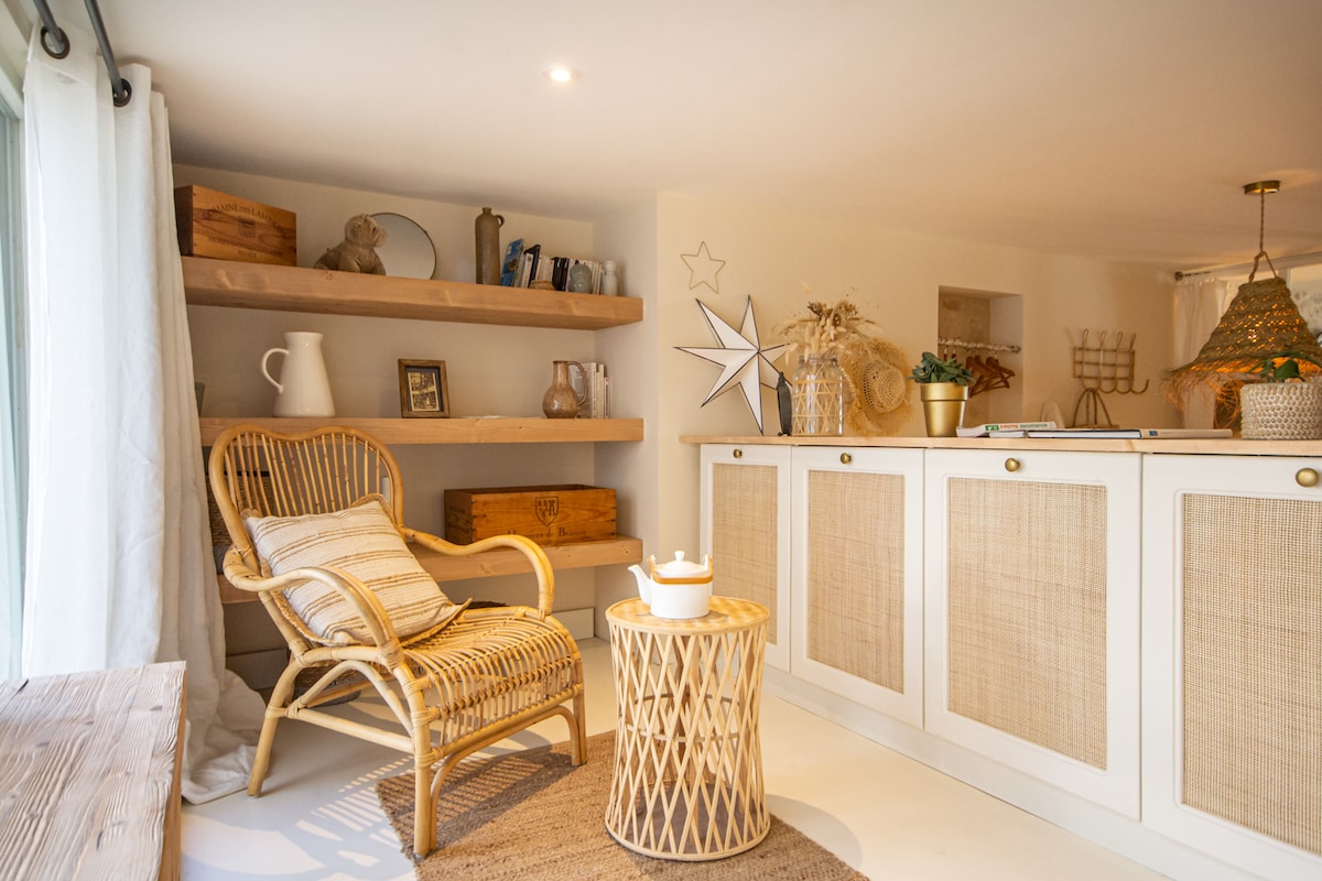 A cozy corner features a rattan chair with a patterned cushion next to a woven coffee table. Open shelves hold decorative items and books, while a neutral-toned rug lies beneath. Soft lighting brightens the space, enhancing its serene atmosphere.