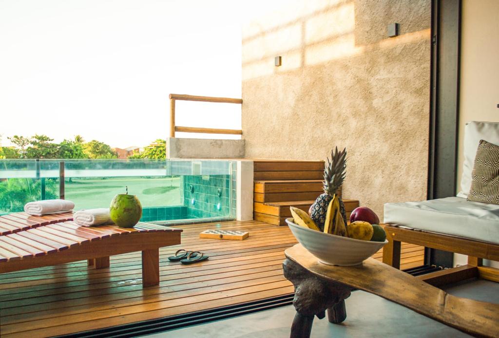 A welcoming outdoor area features wooden decking, complemented by a fruit bowl showcasing an assortment of fresh produce. A lounge chair is positioned nearby, along with towels neatly arranged on a wooden table. Large glass doors offer a view of the lush surroundings.