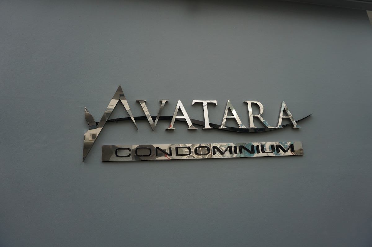 The exterior signage of Avatara Condominium is displayed prominently on a light blue wall. The sign features metallic letters reflecting light, showcasing the name 'Avatara' in a larger font above the word 'Condominium,' which is presented in a contrasting color.