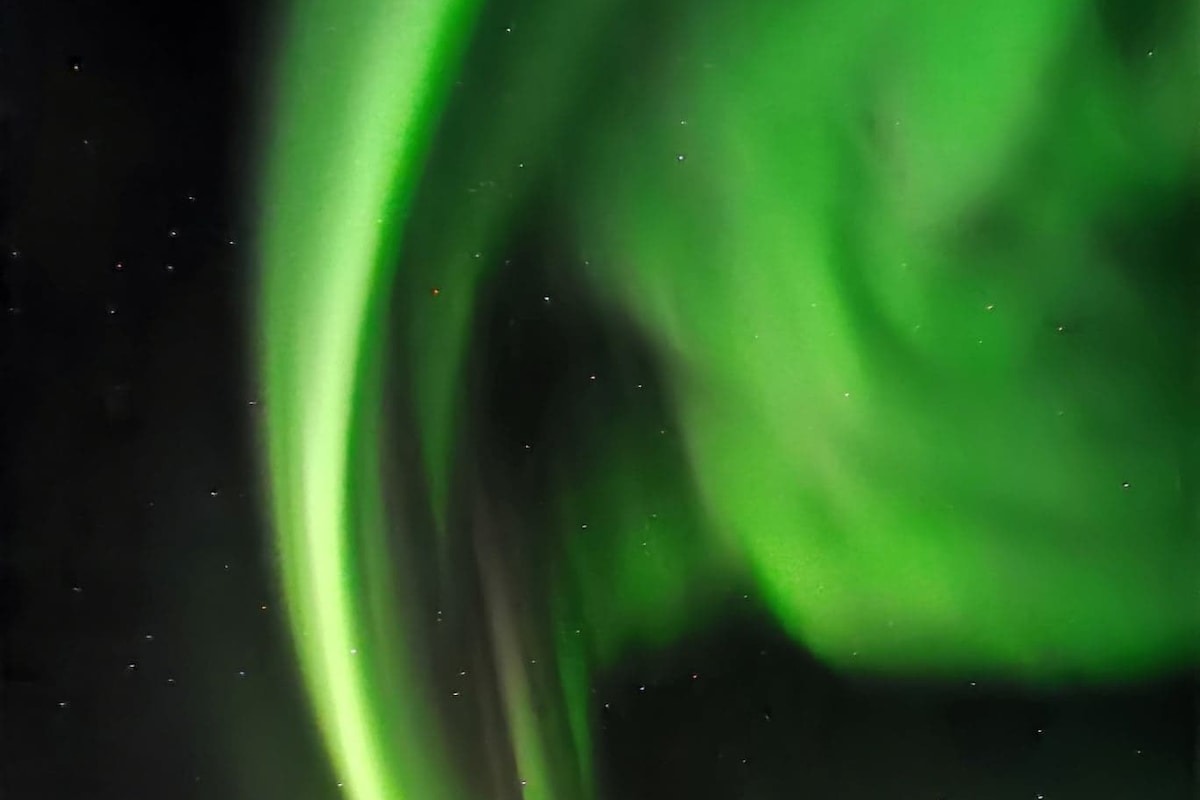 The image captures the northern lights, displaying vibrant green hues swirling against a dark night sky. A subtle starfield is visible in the backdrop, enhancing the natural spectacle of this celestial phenomenon.
