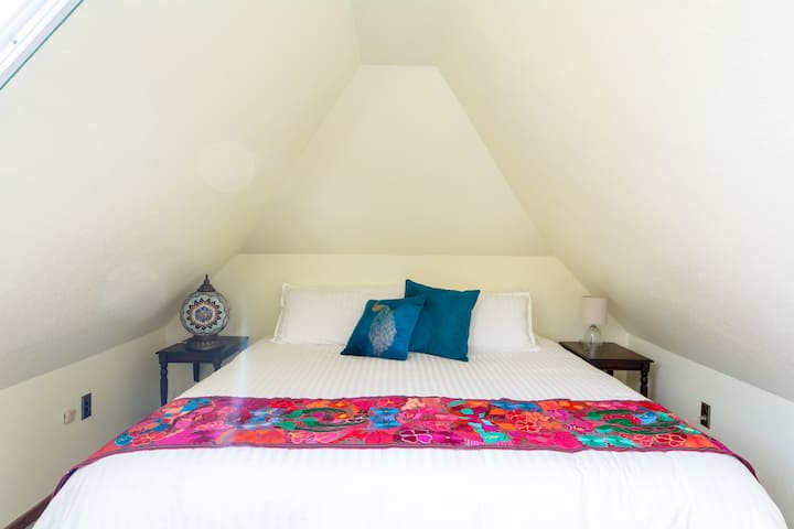 The Onaledge Suite's second room with king bed and sunlight streaming in from the large skylight. This room has a small dresser and is the private bedroom of the Onaledge Suite.