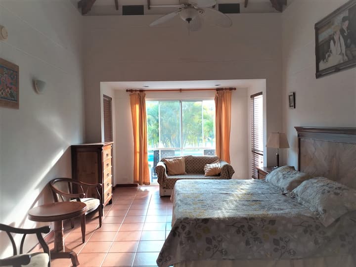 El dormitorio 1, con cama tamaño king, baño privado y vistas a la piscina, es luminoso y acogedor, con una gran ventana que enmarca la exuberante vegetación. Cuenta con cómodos asientos, sofá cama y una decoración de buen gusto. El espacio combina comodidad y encanto, perfecto para un descanso reparador.