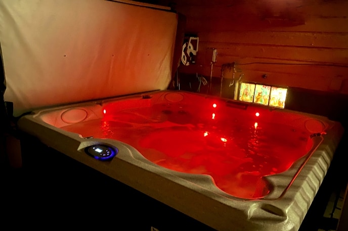 A spacious hot tub is prominently displayed, with red LED lights creating a calming ambiance. The tub is enclosed for privacy and features ergonomic seating. Water gently ripples on the surface, inviting relaxation. Surrounding walls are decorated with subtle artwork, enhancing the overall tranquility of the space.