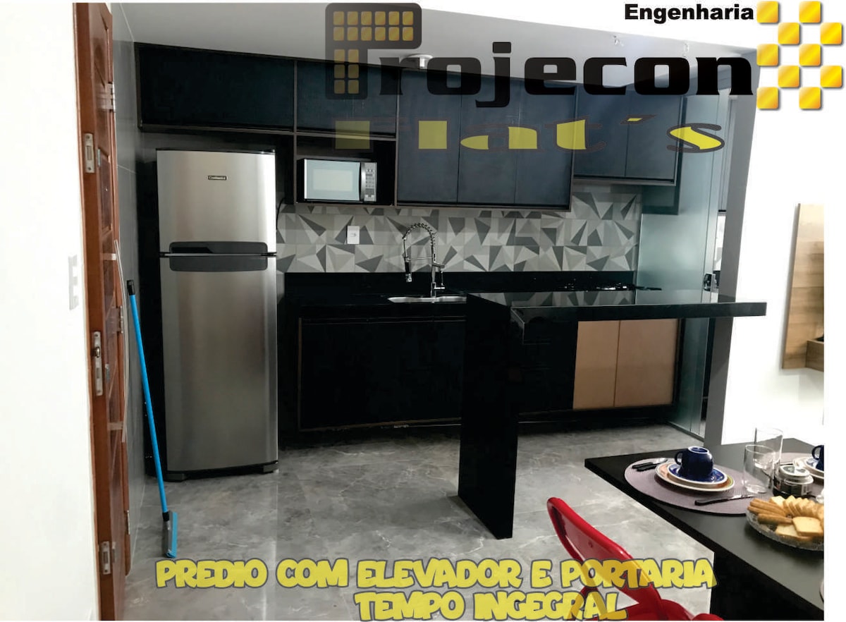 A modern kitchen features sleek black cabinetry and countertops, complemented by stainless steel appliances. A partial wall with geometric tiles adds visual interest. A dining table is set with tableware, indicating a designated eating area, while natural light fills the space through adjacent windows.