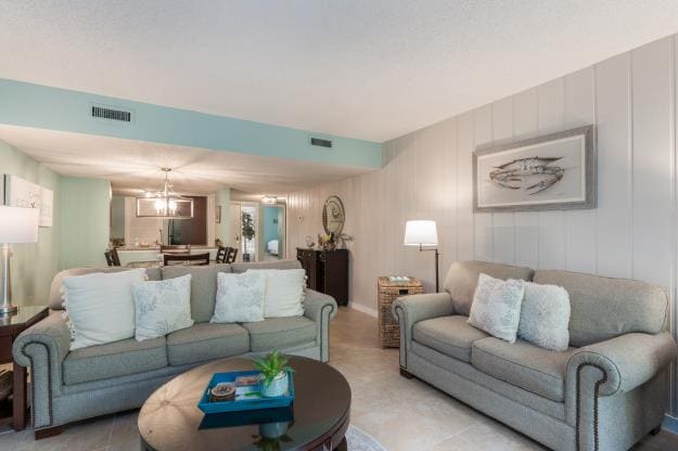 A welcoming living area features a light gray sofa and a matching loveseat, both adorned with decorative pillows. A circular coffee table sits in the center, with a small plant adding a touch of greenery. Soft lighting is provided by floor lamps, enhancing the cozy ambiance.