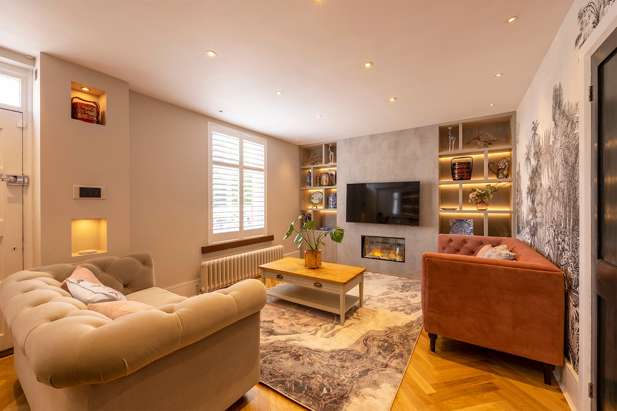 A modern living area showcases a light-colored couch paired with a plush armchair. A wooden coffee table occupies the center, while a large flat-screen TV is mounted on the wall. Soft lighting highlights the decorative shelving, creating a cozy ambiance.