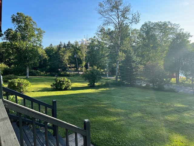 A lush green lawn stretches out under clear blue skies, framed by a variety of trees. The space features well-maintained garden areas, creating a peaceful outdoor setting ideal for relaxation.