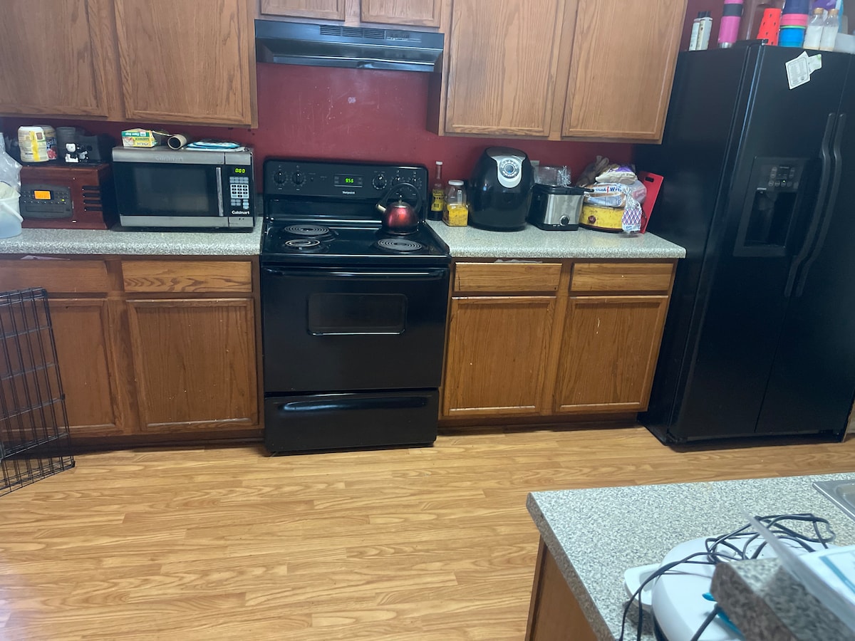 A well-equipped kitchen features wooden cabinetry and a deep black stove. Counter space is available for meal prep, complemented by a microwave and coffee maker. A black refrigerator stands nearby, with various cooking essentials visible on the counter.
