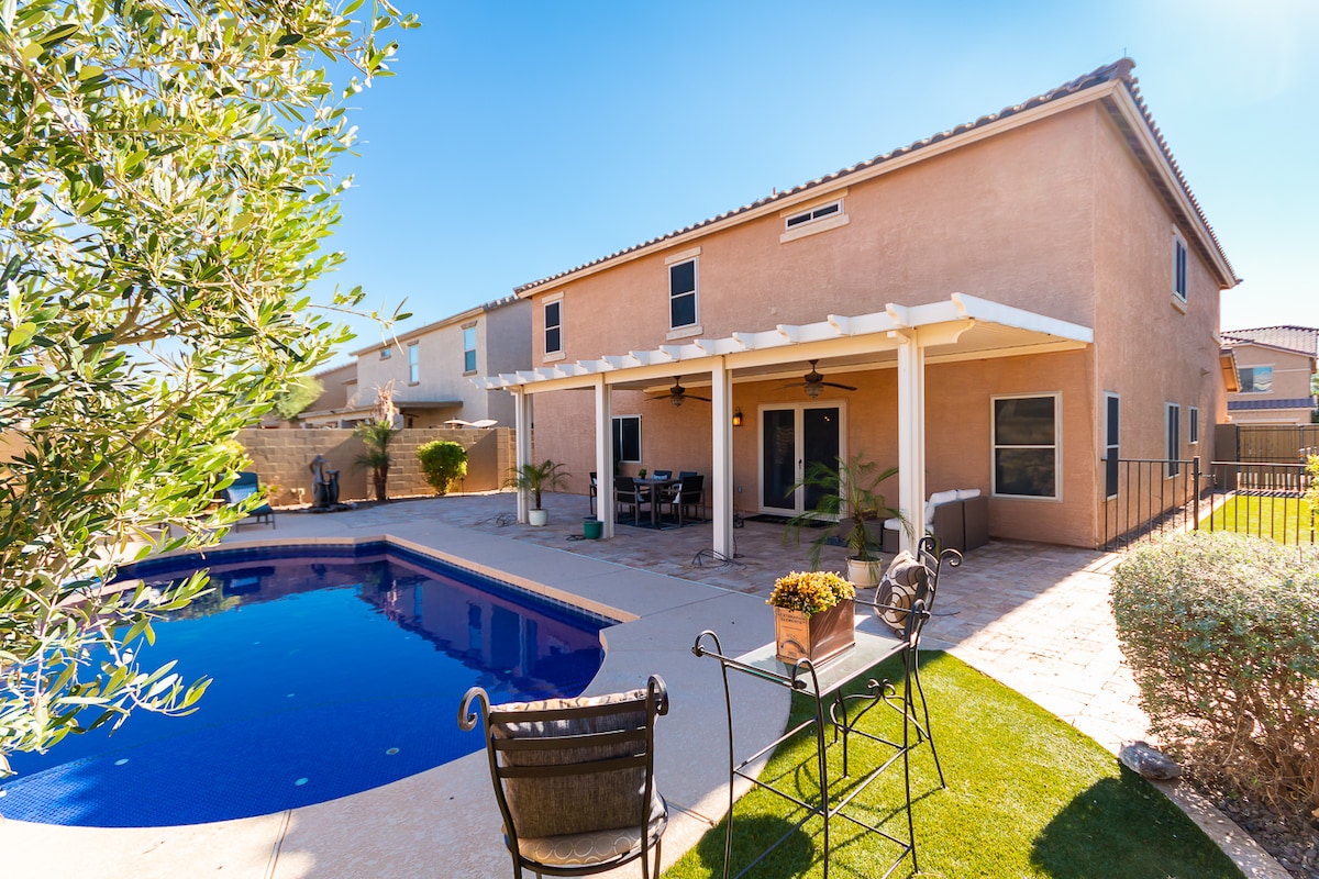 The backyard features a well-maintained heated pool surrounded by a paved patio area. A covered seating area is highlighted by ceiling fans, and potted plants add greenery. The property is enclosed by a fence, providing a private outdoor space.