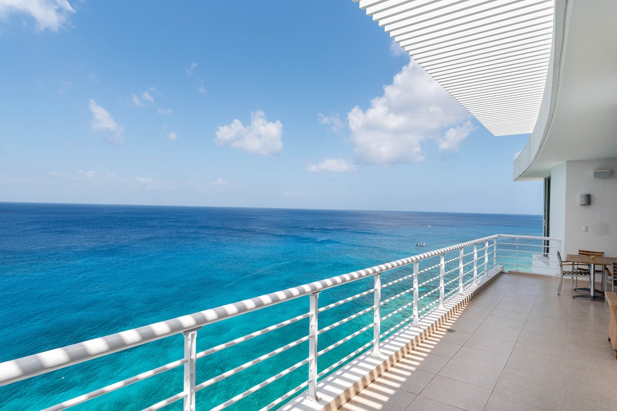 A spacious terrace offers unobstructed views of the azure ocean and distant horizon. Railing with horizontal slats enhances the sense of openness. Natural light floods the area, with a clean tile floor providing a seamless transition to the outdoor space.
