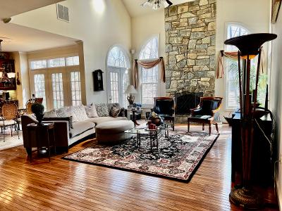 An inviting living area features a mix of comfortable seating, including a sectional couch and two armchairs, arranged around a decorative coffee table. A stone fireplace serves as a focal point, while large windows allow natural light to fill the space. Wooden floors enhance the warm ambiance.