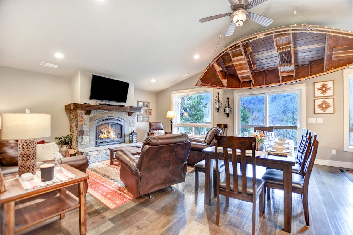 A cozy living and dining area is showcased, featuring a stone fireplace as the focal point. Comfortable leather chairs are arranged around a wooden dining table, set for a meal. A unique wooden ceiling element mimics the shape of a boat, adding character to the space.