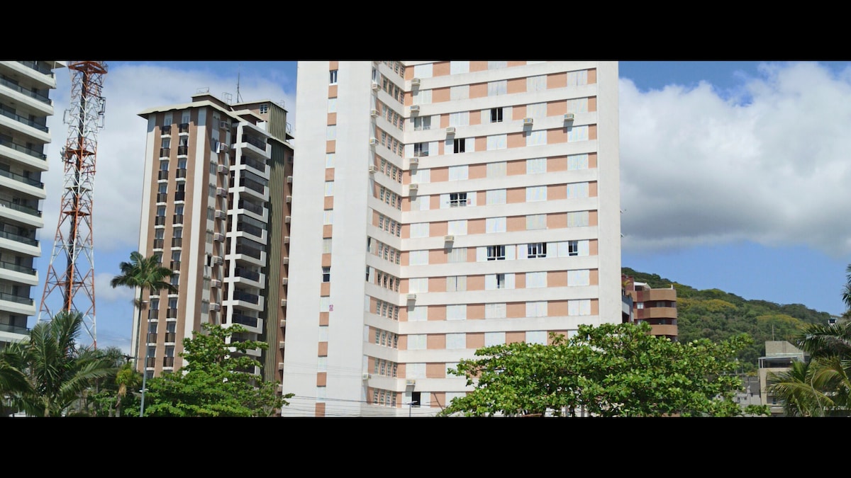 The image displays a collection of modern residential buildings surrounded by greenery. A telecommunications tower is visible in the foreground, with multiple windows reflecting the sky. The architecture showcases a mix of light and darker colors, contributing to the urban landscape.