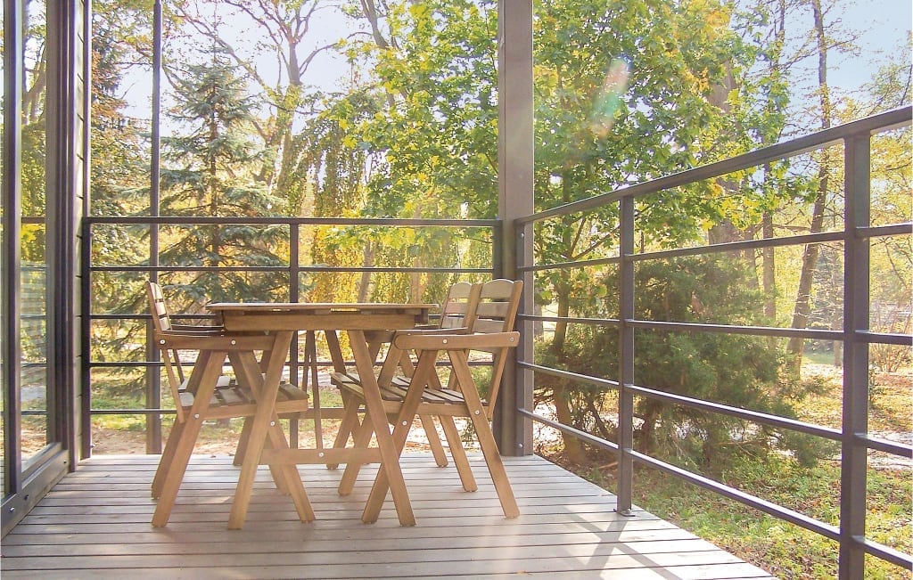 A wooden table is surrounded by four foldable chairs on a sunlit terrace. The railing offers views of lush greenery, creating a connection to nature while providing a comfortable outdoor space for dining or relaxation.