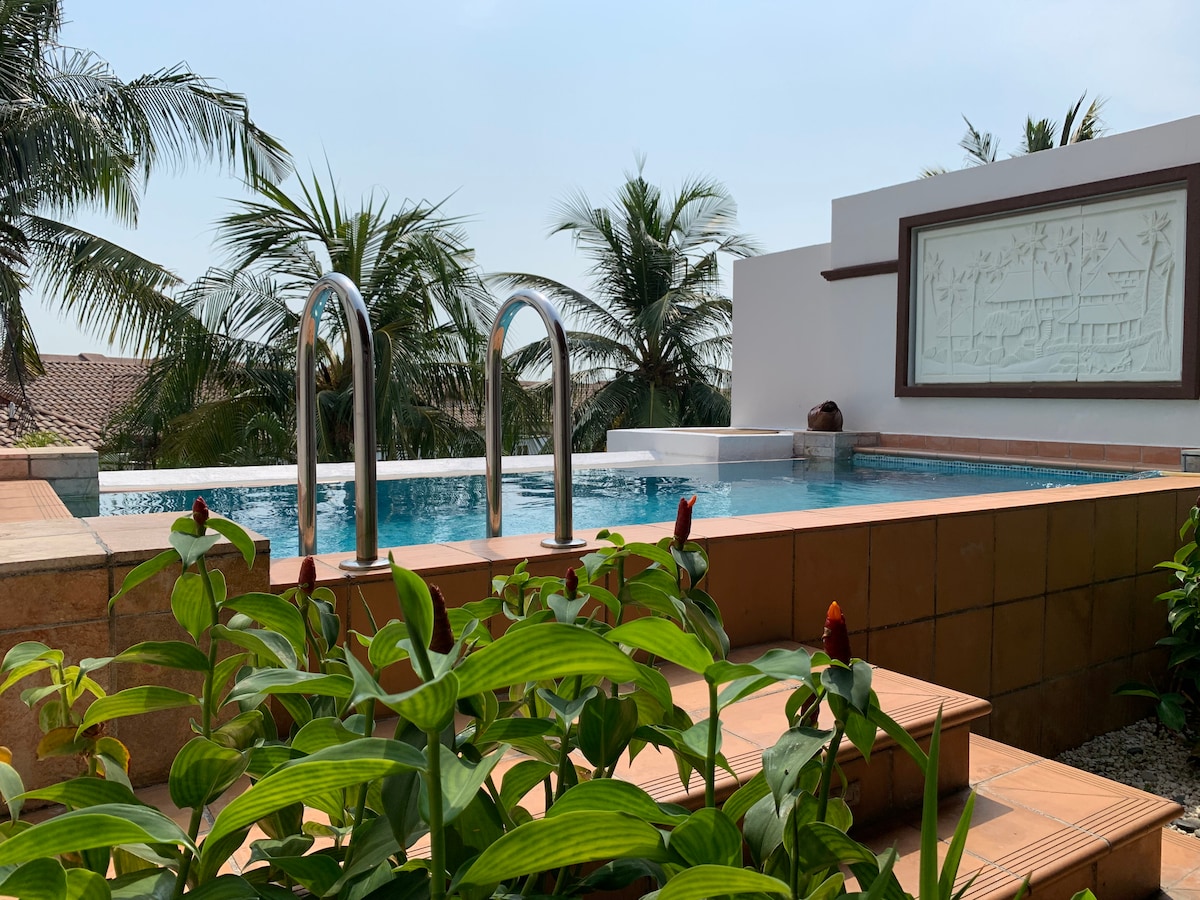 The image showcases a private pool surrounded by tropical greenery, with clear water inviting leisurely swims. Lush plants frame the area, while palm trees provide a natural backdrop, contributing to a serene and relaxing environment.